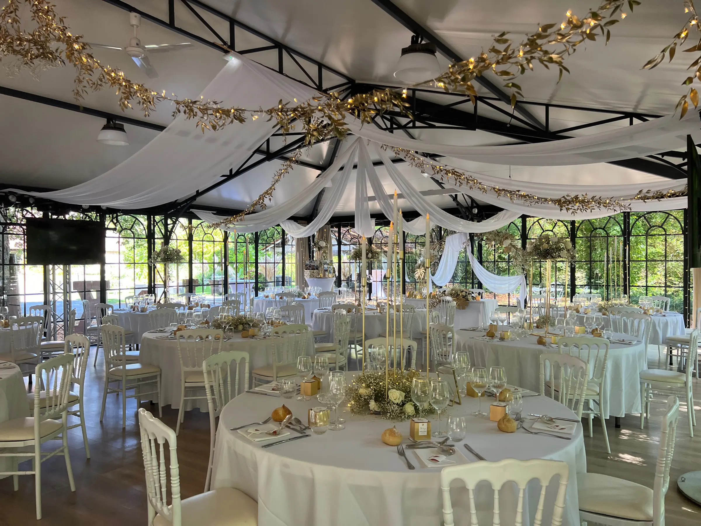 Salle de réception de mariage décorée par Armony's Déco : voilages, guirlandes lumineuses et centres de table dorés