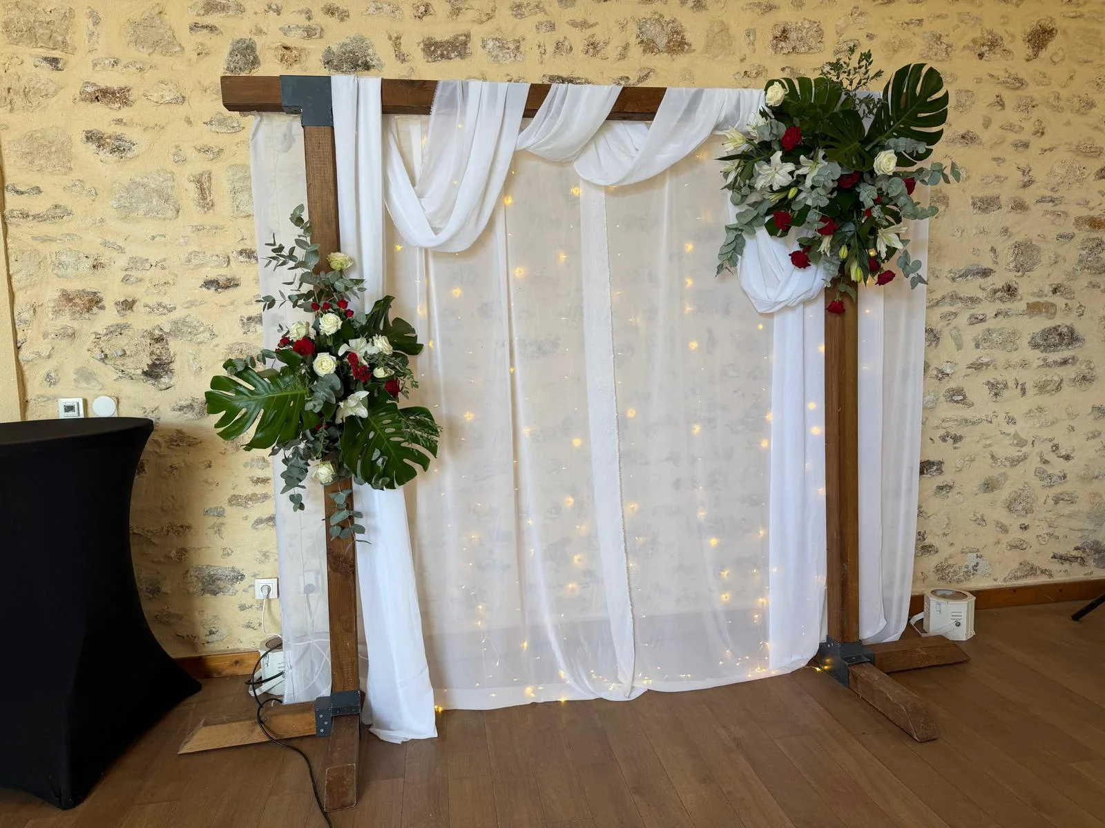 Photobooth : arche en bois, voilage blanc, rideau lumineux, roses rouges, lys et monstera – Armony's Déco