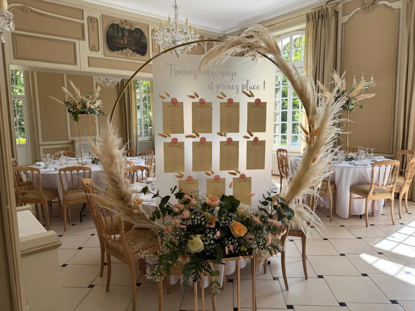 Plan de table « Trouvez votre siège » sur cerceau doré avec pampa et roses pêche – Armony's Déco