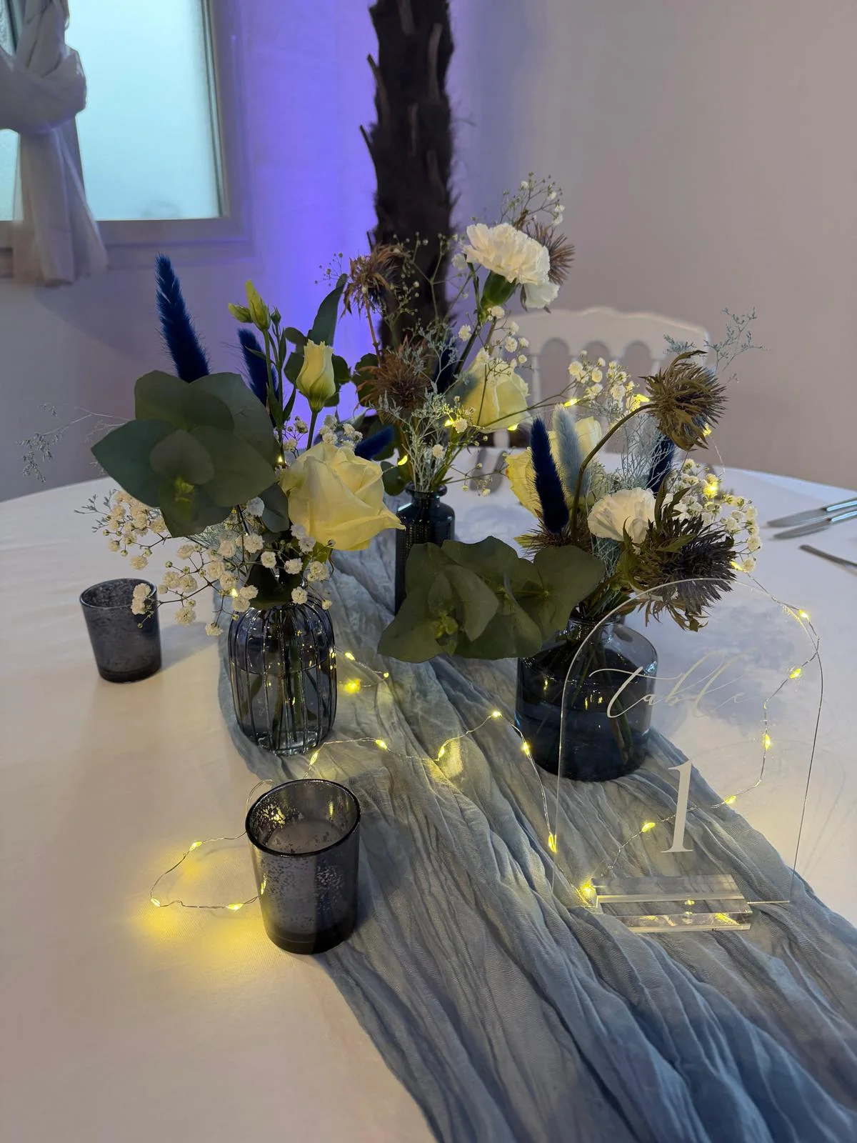 Fioles bleu nuit, fleurs blanches et guirlande lumineuse sur chemin de table bleu – Armony's Déco