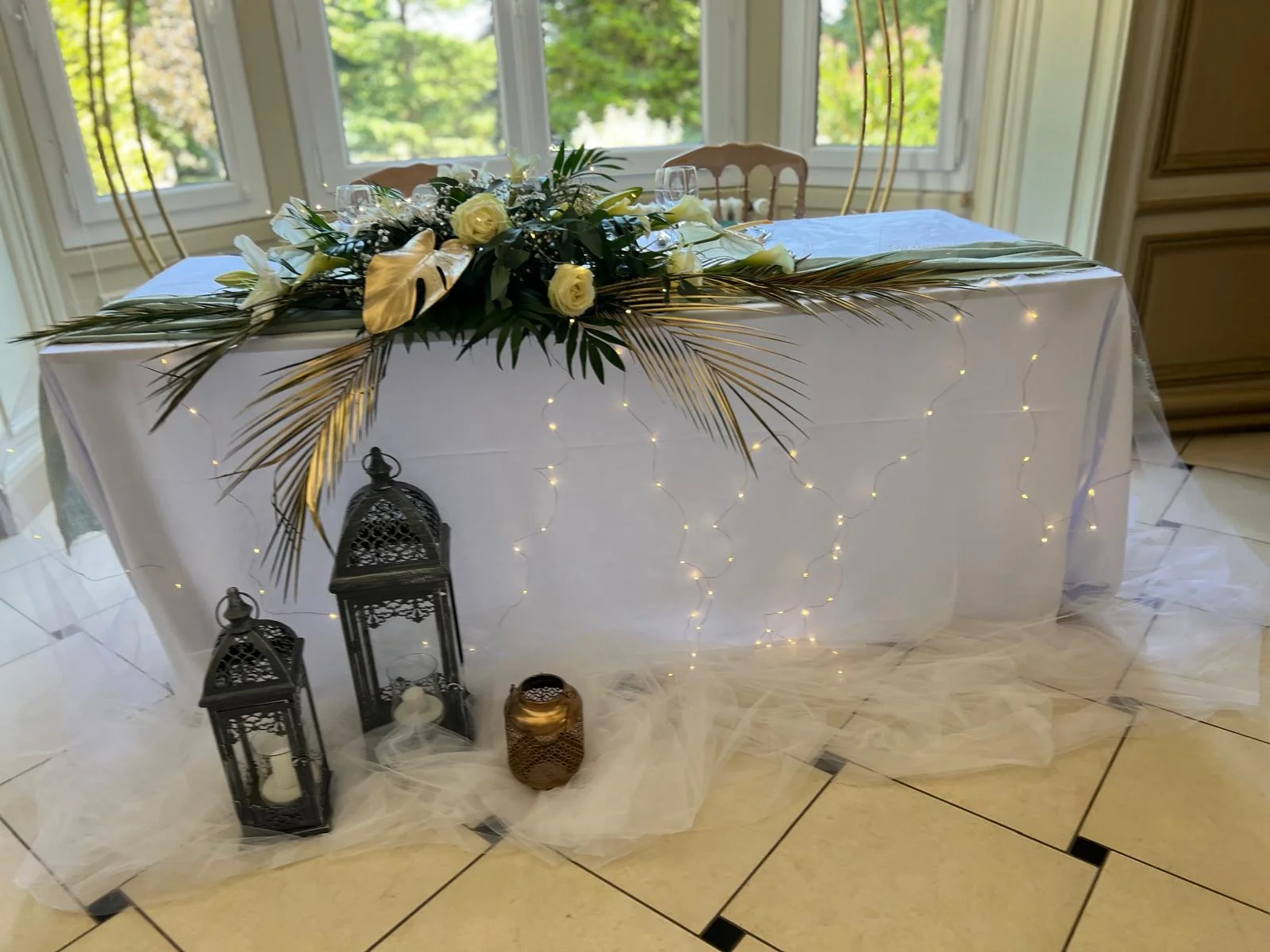 Table d'honneur aux lanternes, voilage lumineux et feuilles de palmier dorées – Armony's Déco