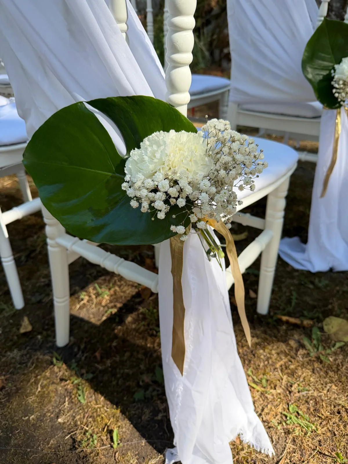 Chaise de cérémonie décorée d'un œillet blanc, gypsophile et feuille de monstera, ruban doré – Armony's Déco