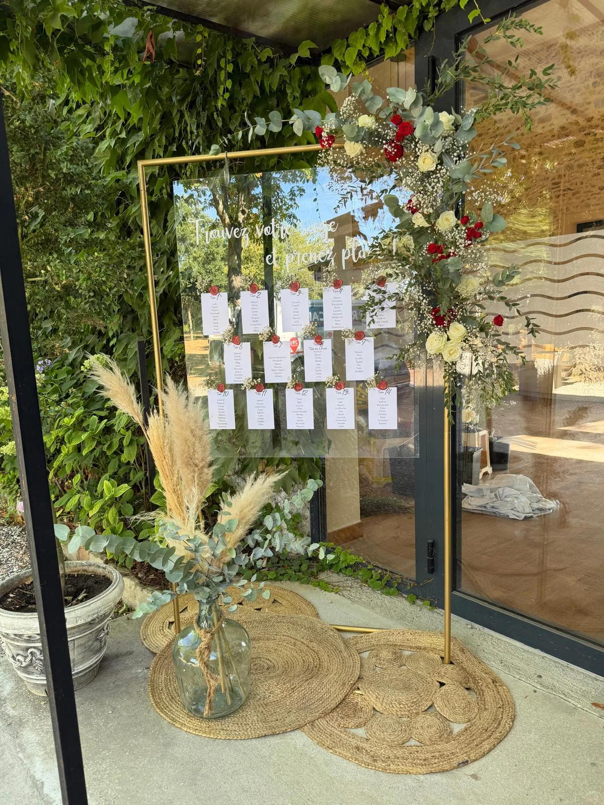 Plan de table sur structure dorée, pampa et roses rouges devant un mur végétal – Armony's Déco