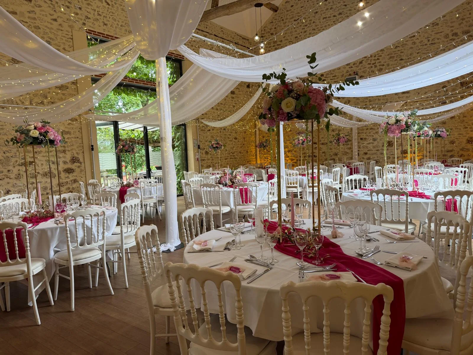 Salle de réception aux voilages blancs, centres de table hauts et chemins de table rouges – Armony's Déco